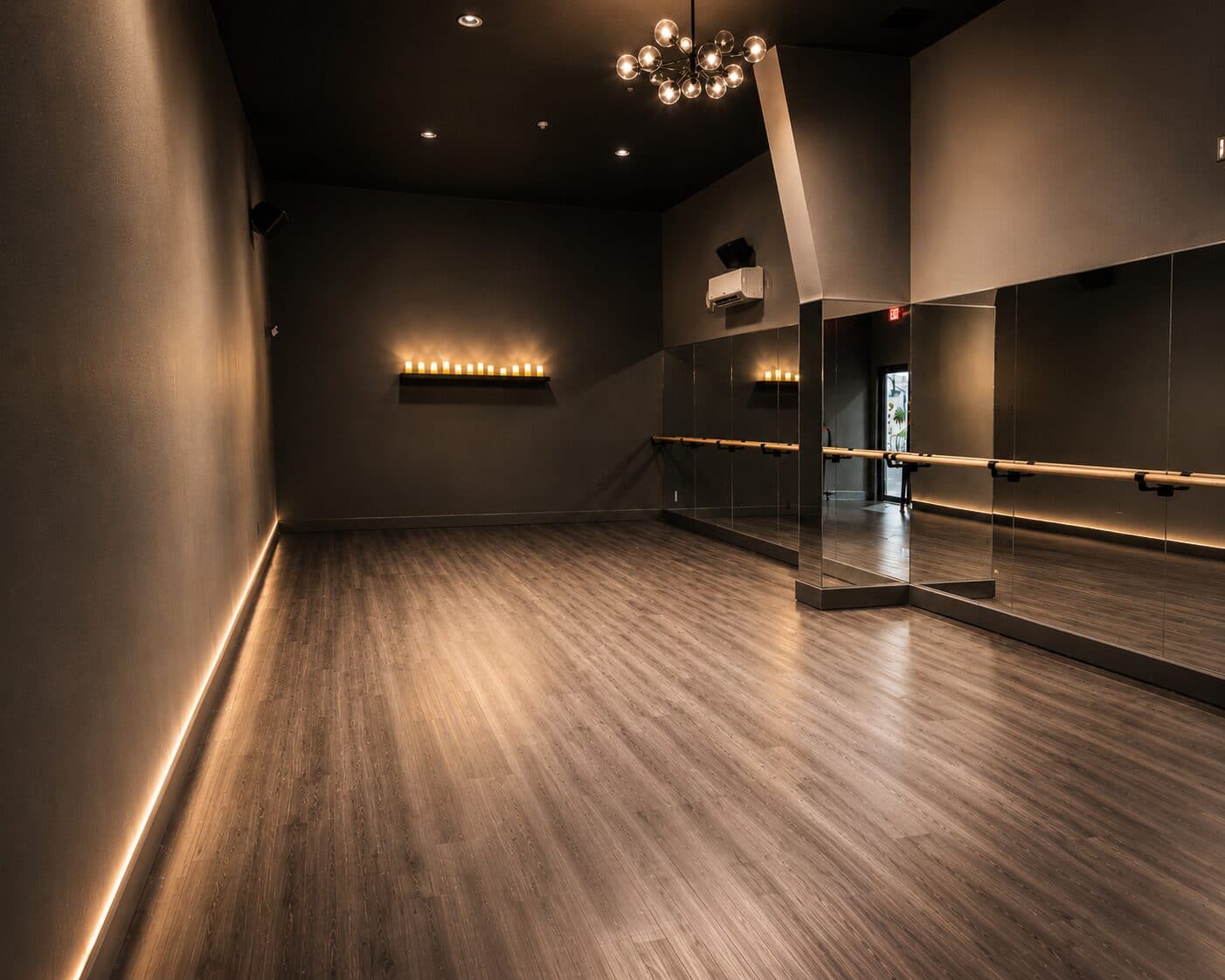 Group fitness and movement studio at Sanctuary Fitness, with hardwood floors, a mirrored wall, and a statement chandelier.